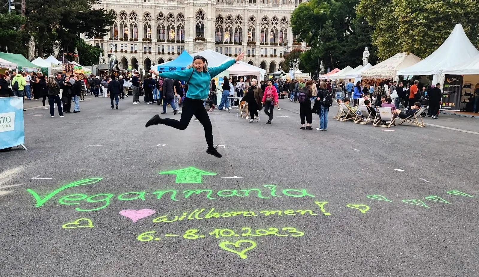 Claire mid-jump in front of the Vegan Mania market sign in Vienna