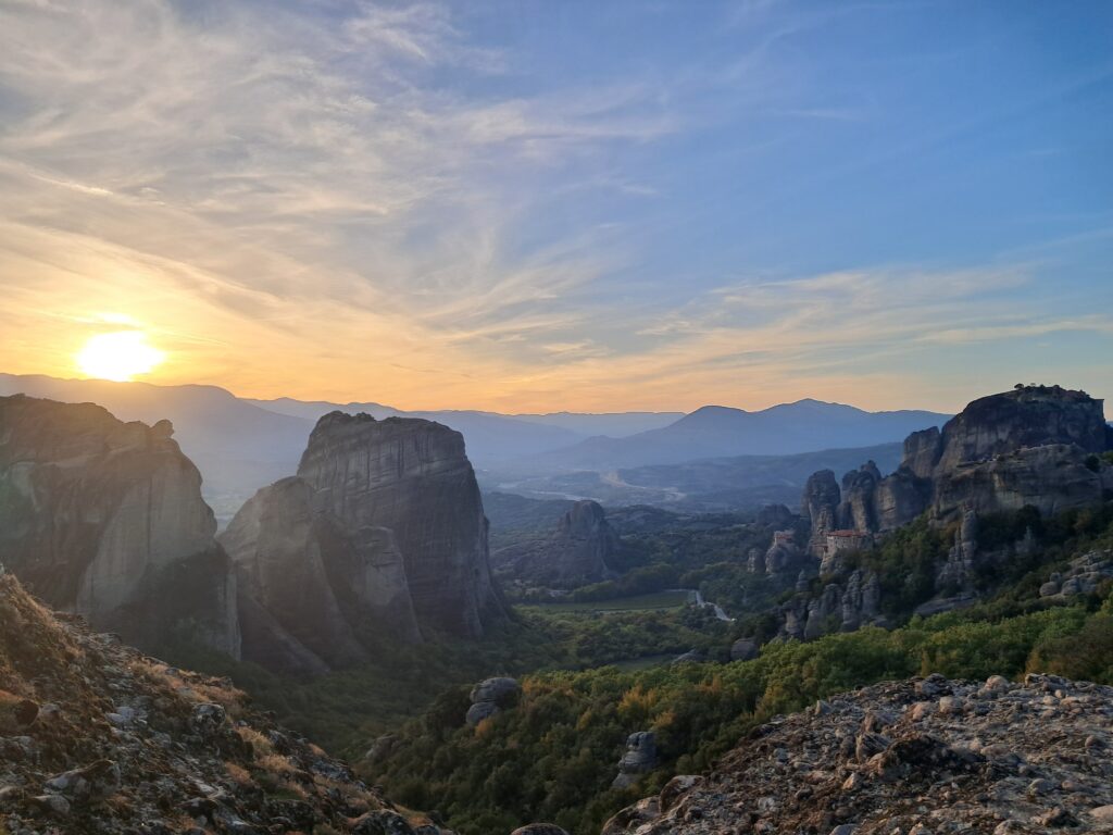 Meteora rock formations and monasteries silhouetted against a golden sunset, viewed from above Kalambaka, Greece