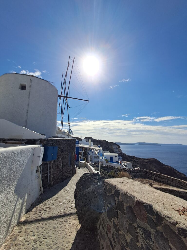 A traditional windmill and cobbled street in Oia, Santorini, with the caldera visible in the background
