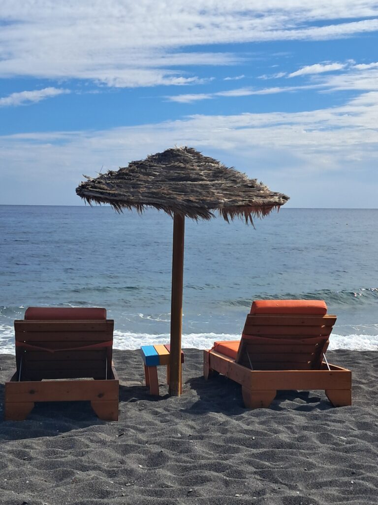 Sun loungers on the black volcanic sand beach at Perissa, Santorini, easily reached thanks to having a hire car