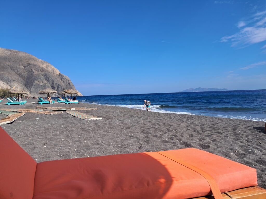 Black sand beach at Perissa, Santorini, with sun loungers and cliffs in the background
