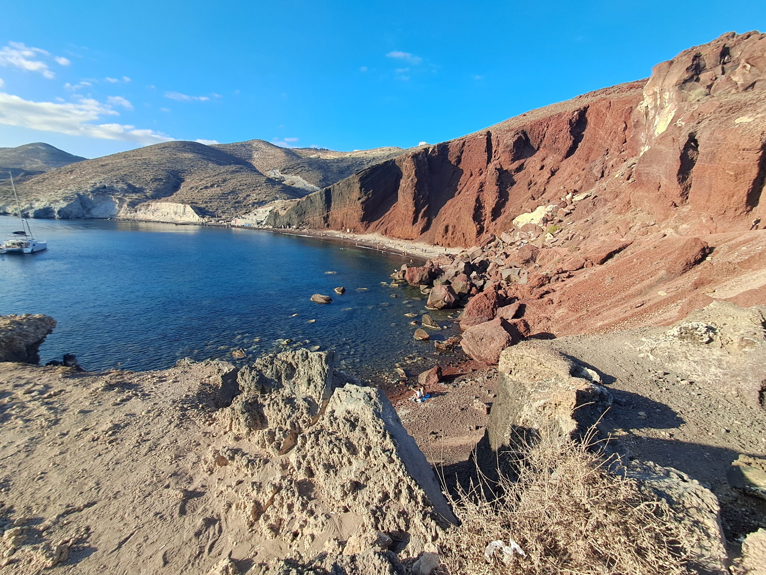 Dramatic red volcanic cliffs of Red Beach in Santorini with boats on the blue Aegean Sea below