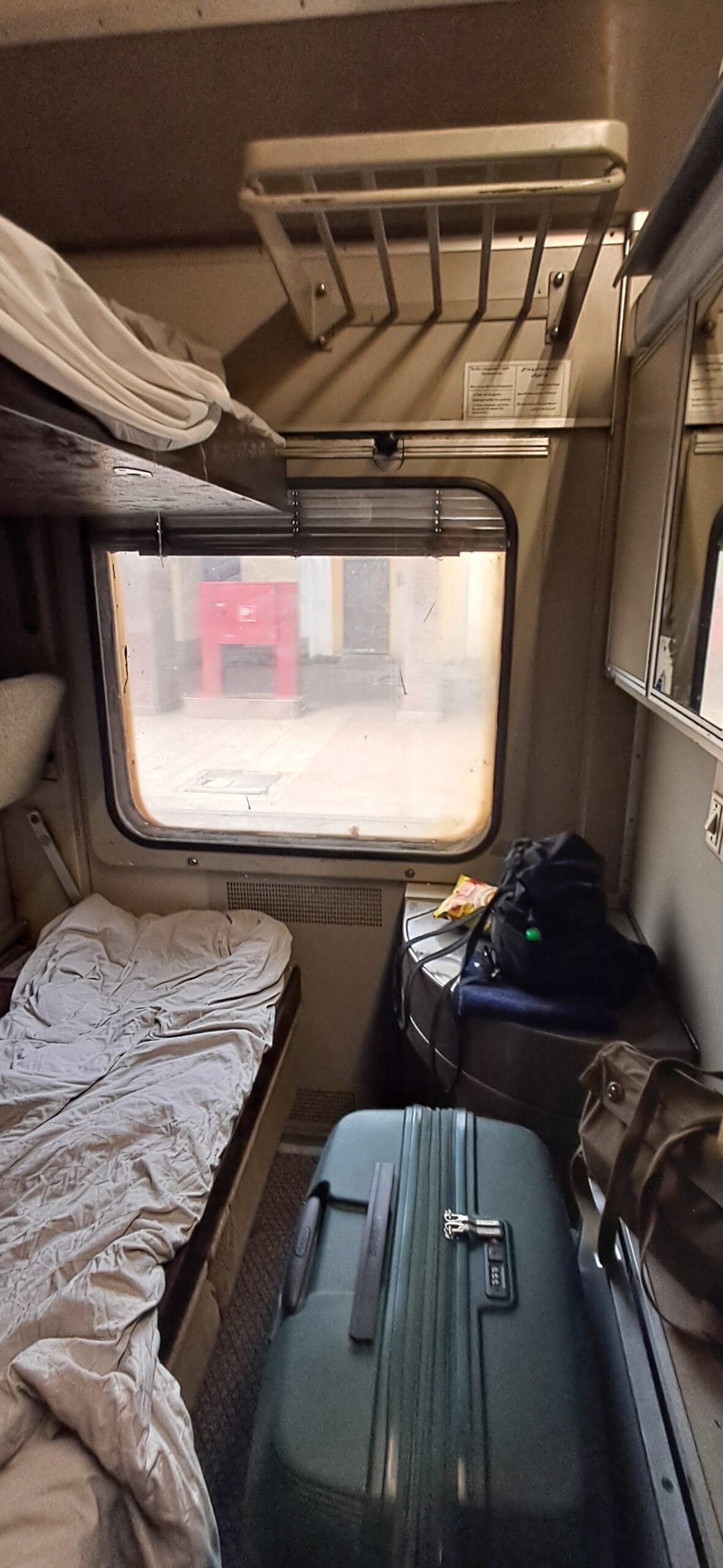 Inside a cabin on the Egypt sleeper train, with the window, a fold-down rack and a suitcase