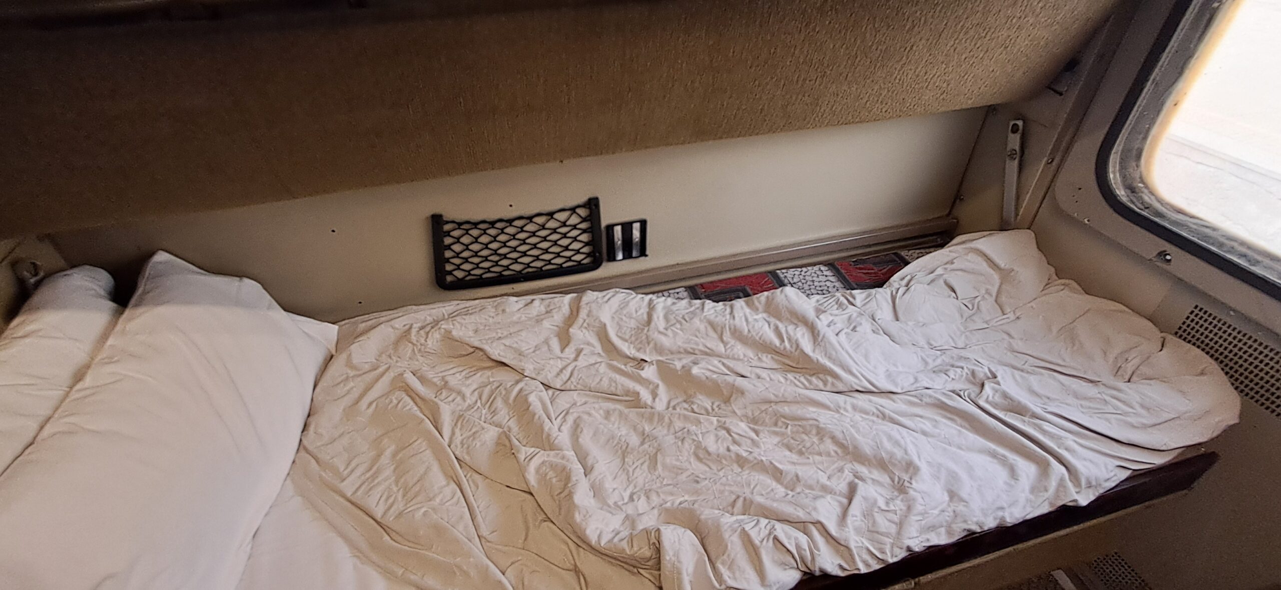 A made-up bunk bed with white sheets and a pillow in an Egypt sleeper train cabin