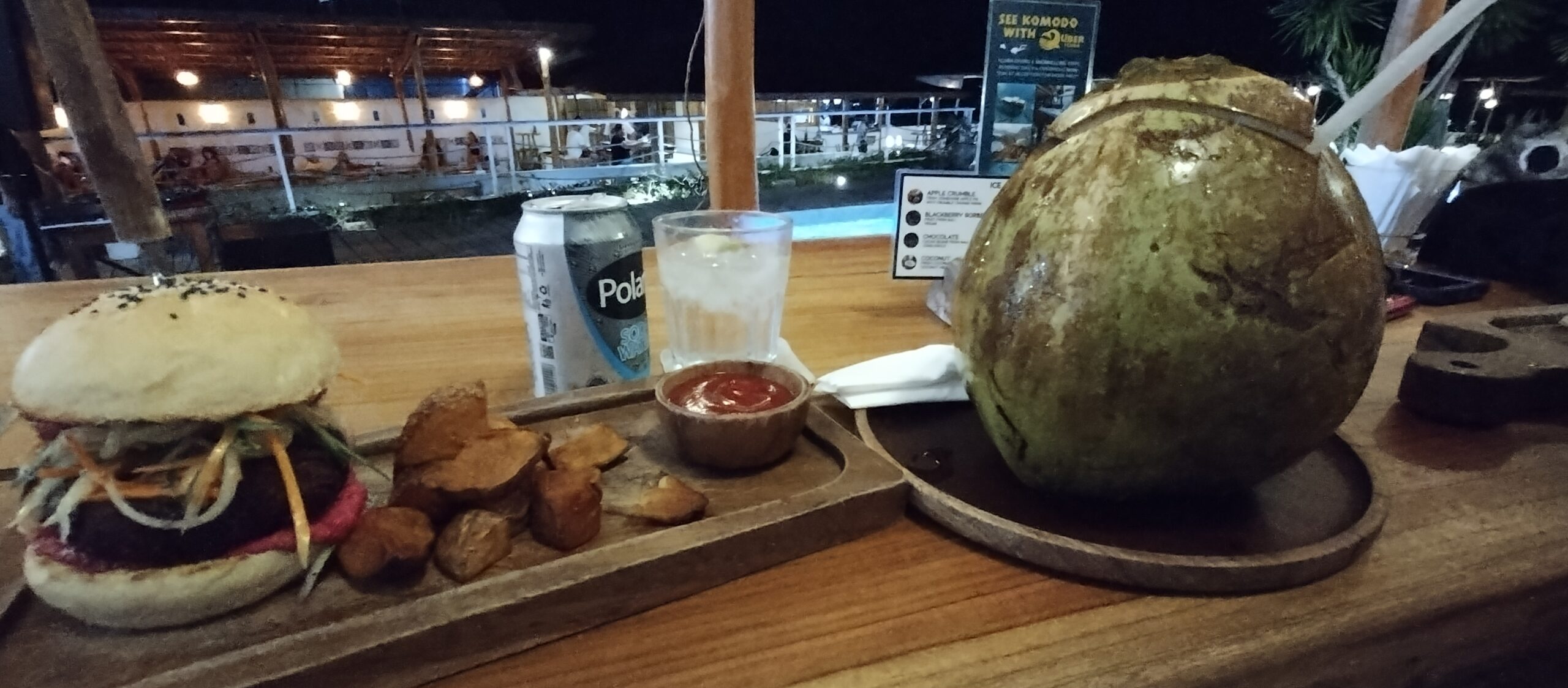 Vegan burger and a fresh coconut on a wooden board at Seaesta Komodo