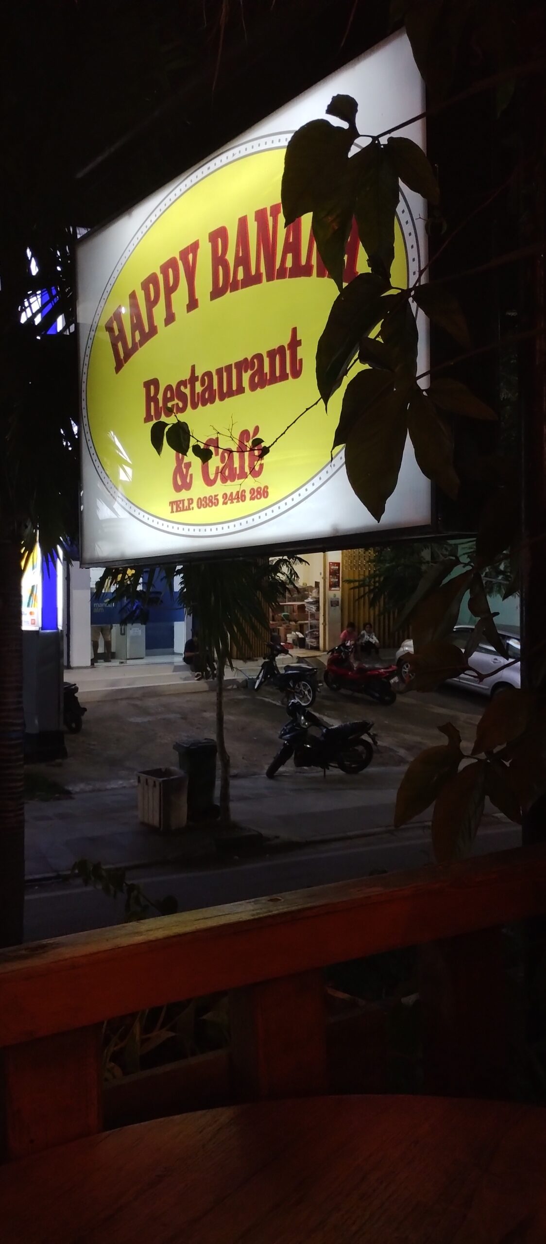 The Happy Banana Komodo restaurant sign lit up at night