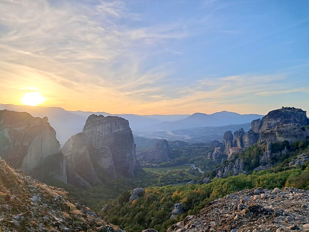 Meteora rock formations and monasteries silhouetted against a golden sunset, viewed from above Kalambaka, Greece