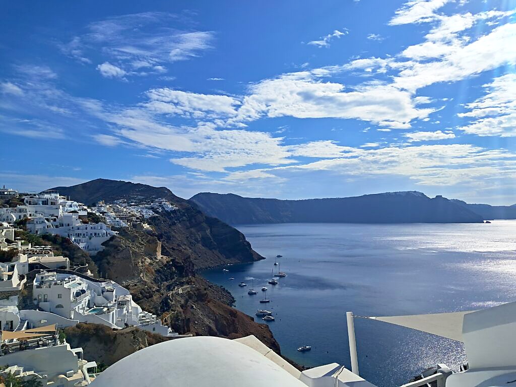 View over the Santorini caldera from Oia, with white cliffside buildings and boats anchored in the bay below