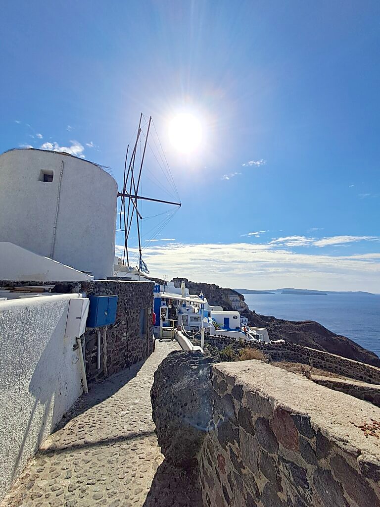 A traditional windmill and cobbled street in Oia, Santorini, with the caldera visible in the background