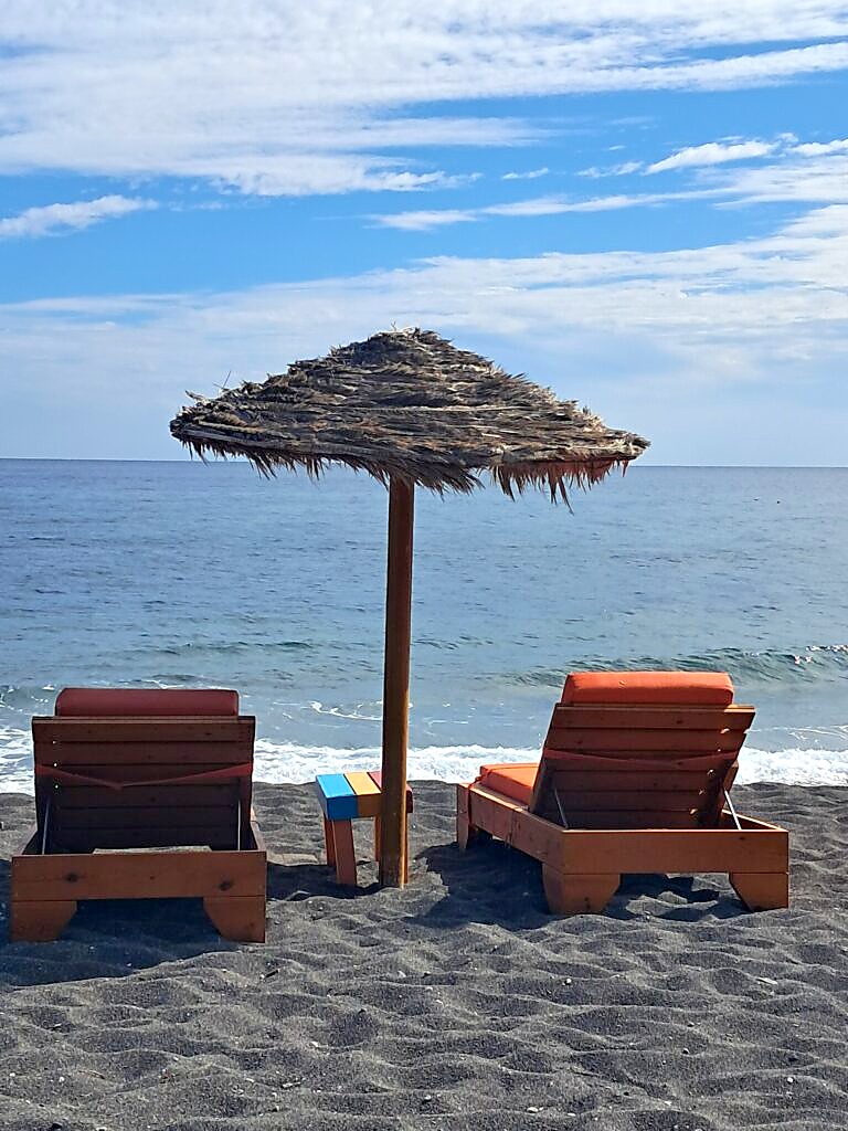 Sun loungers on the black volcanic sand beach at Perissa, Santorini, easily reached thanks to having a hire car