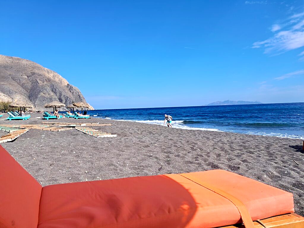 Black sand beach at Perissa, Santorini, with sun loungers and cliffs in the background