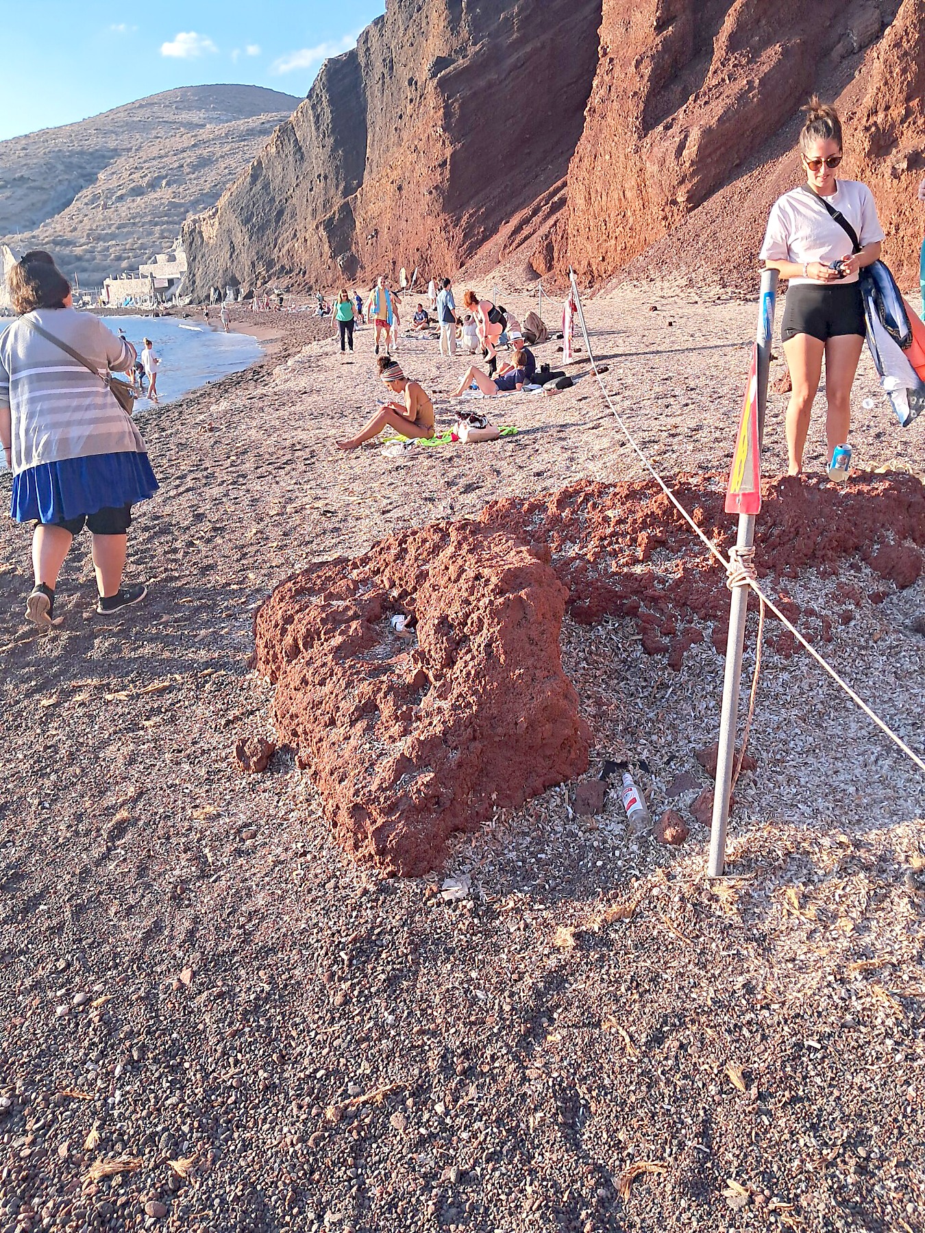 Roped-off cordon beneath the cliffs at Red Beach, Santorini, with people sitting behind it